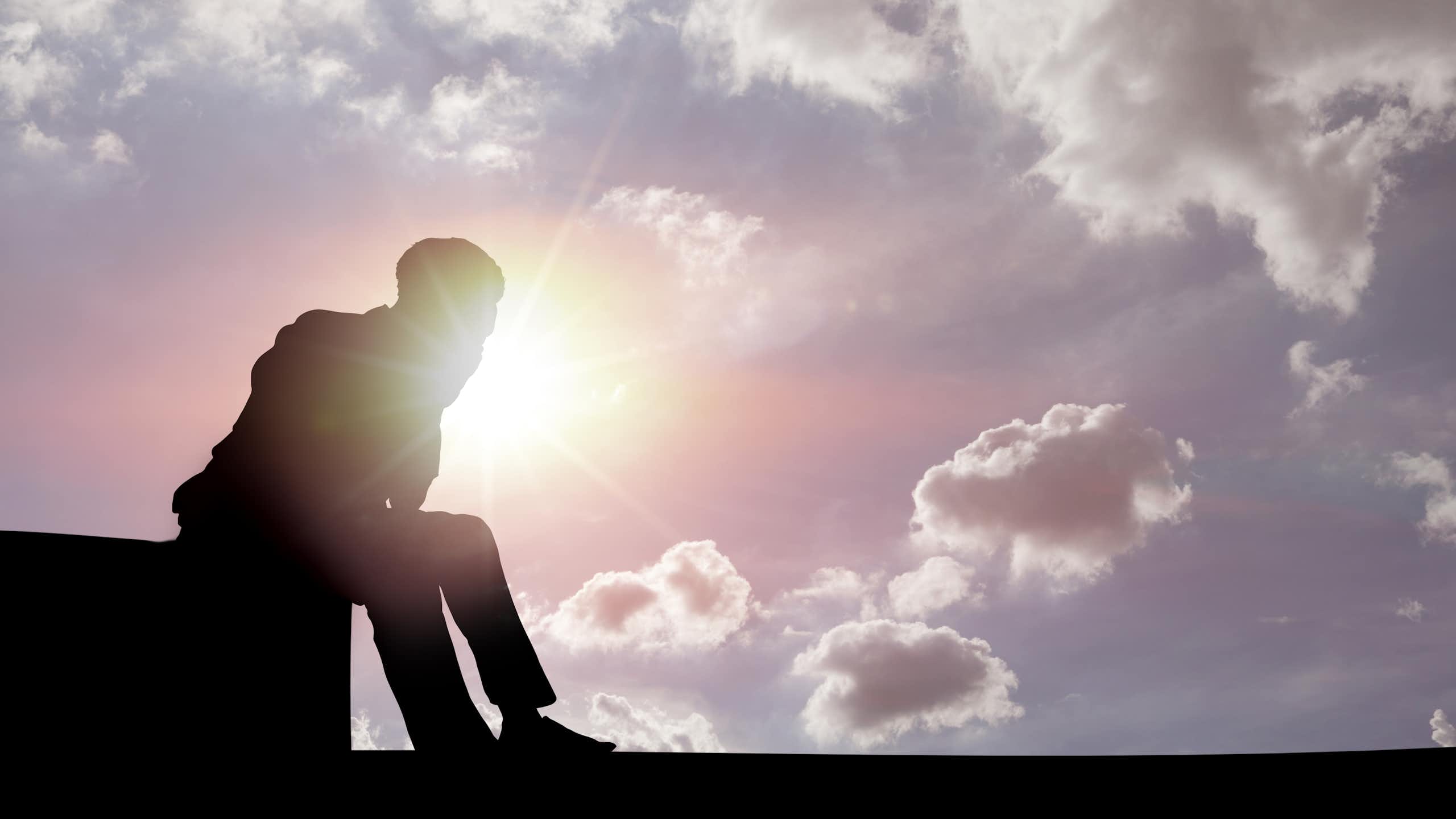 silhouette of a man sitting on a structure against a bright sunny sky