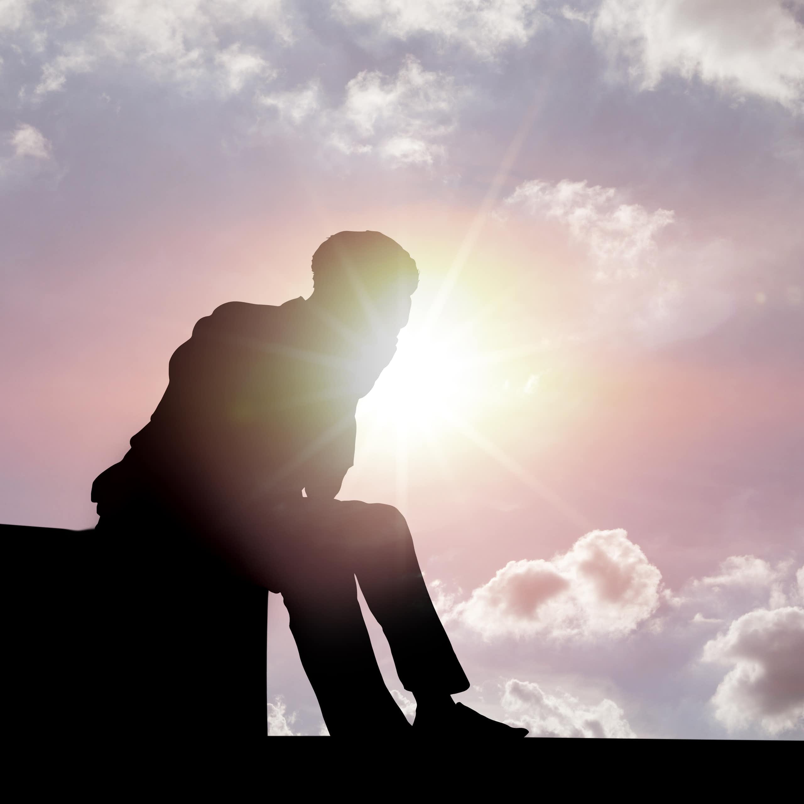 silhouette of a man sitting on a structure against a bright sunny sky