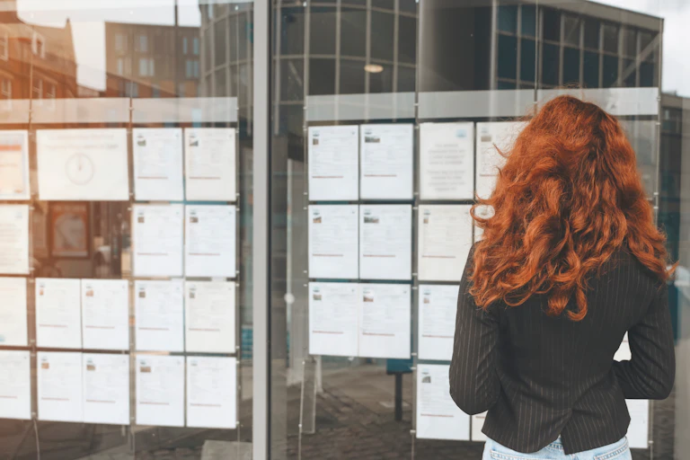 woman with long red hair reading notices on a jobs board.