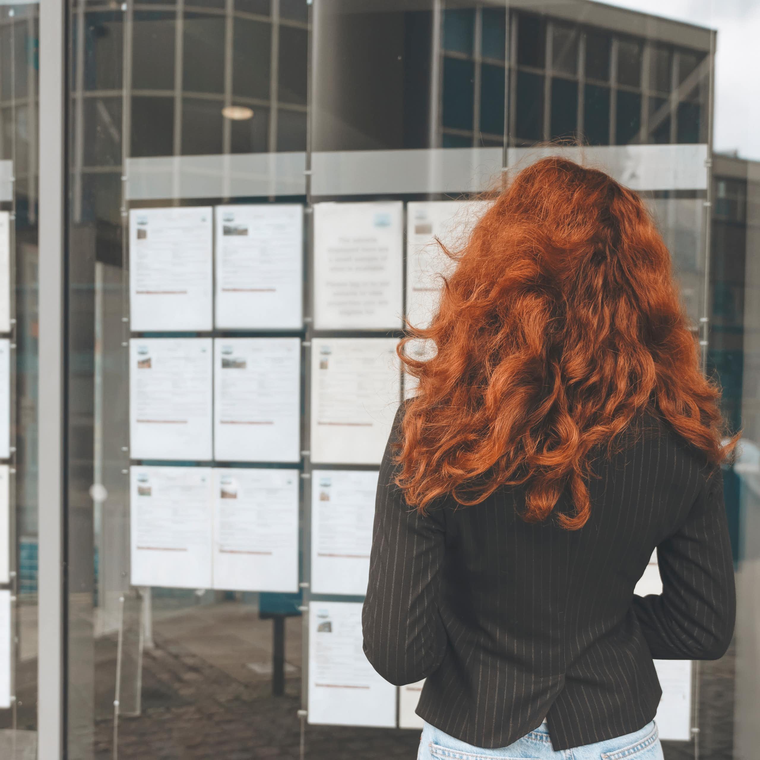 woman with long red hair reading notices on a jobs board.