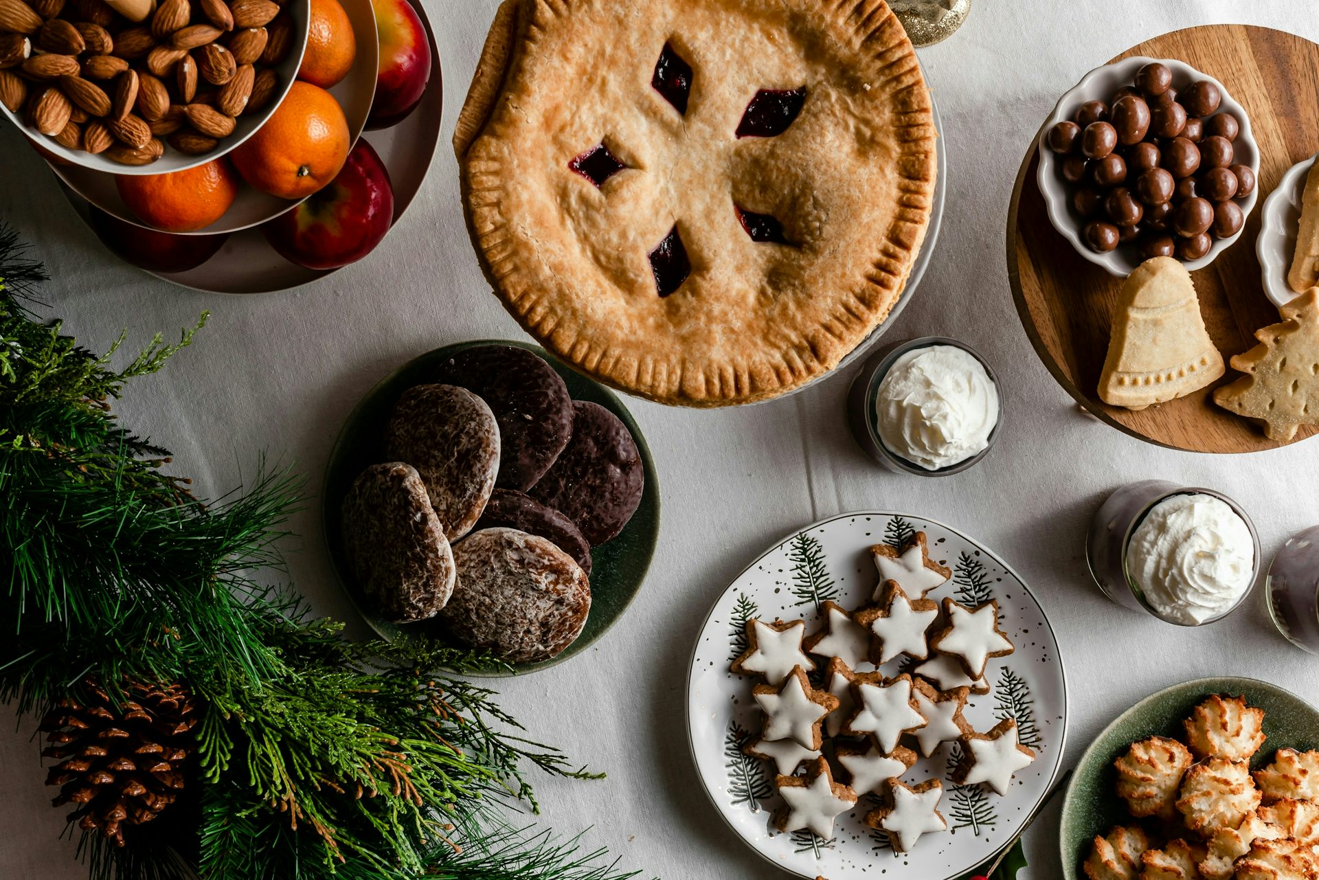 Une sélection de desserts, de fruits et de noix sur une table, accompagnée d’une branche de sapin.