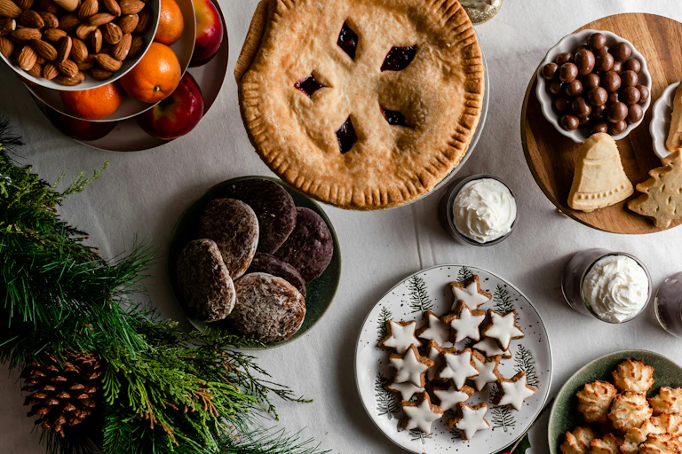 Une sélection de desserts, de fruits et de noix sur une table, accompagnée d’une branche de sapin.