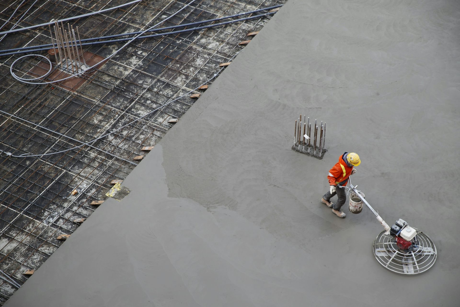 A person in a hi-vis jacket and hard hat moves across a large concrete surface with a power trowel.