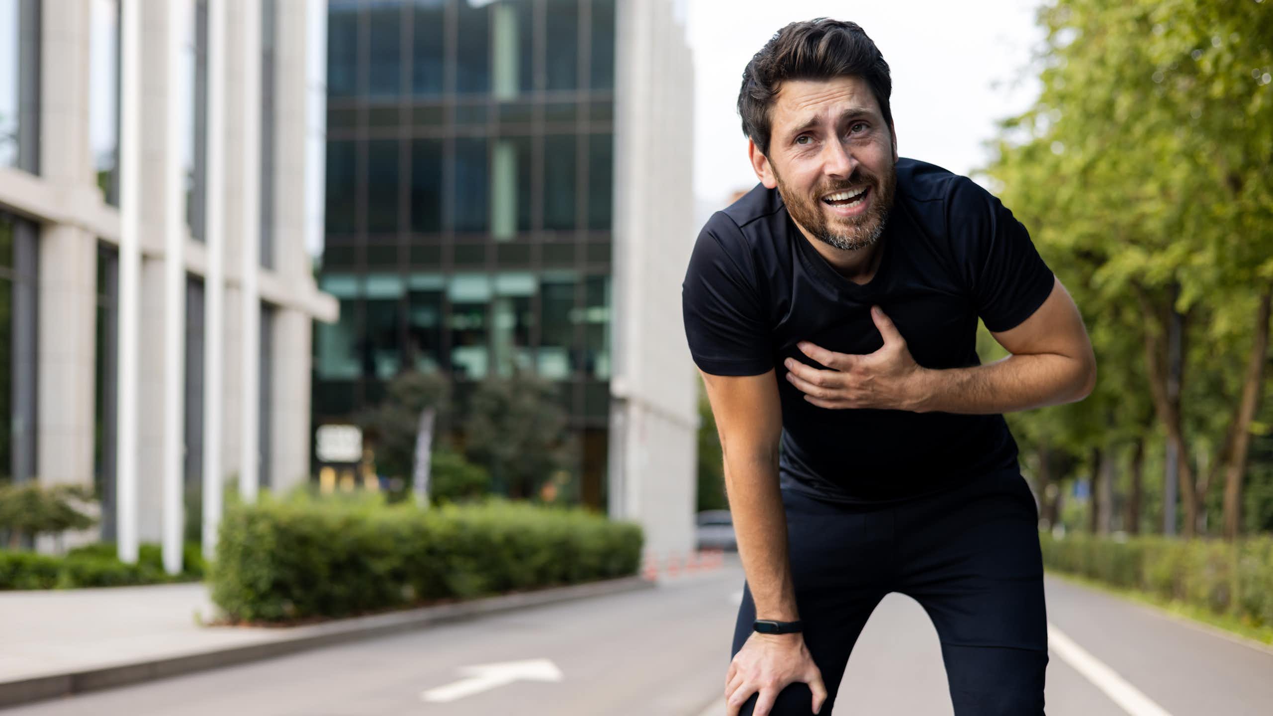 Photo d’un homme en tenue de sport, penché en avant, la main posée sur la poitrine, semblant éprouver des difficultés.