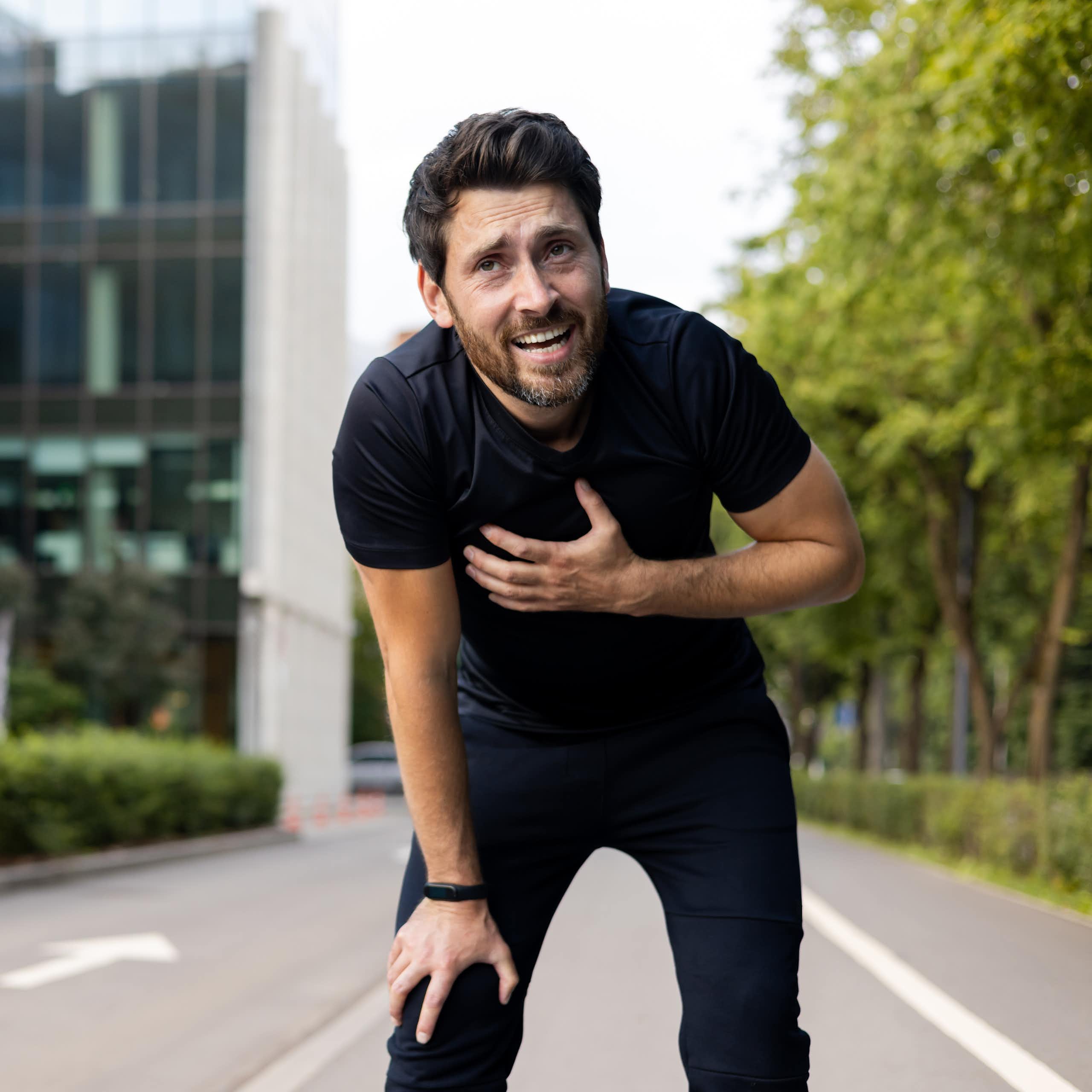 Photo d’un homme en tenue de sport, penché en avant, la main posée sur la poitrine, semblant éprouver des difficultés.