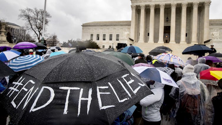 A person holds an umbrella that reads '#EndTheLies' during a rally outside the Supreme Court.