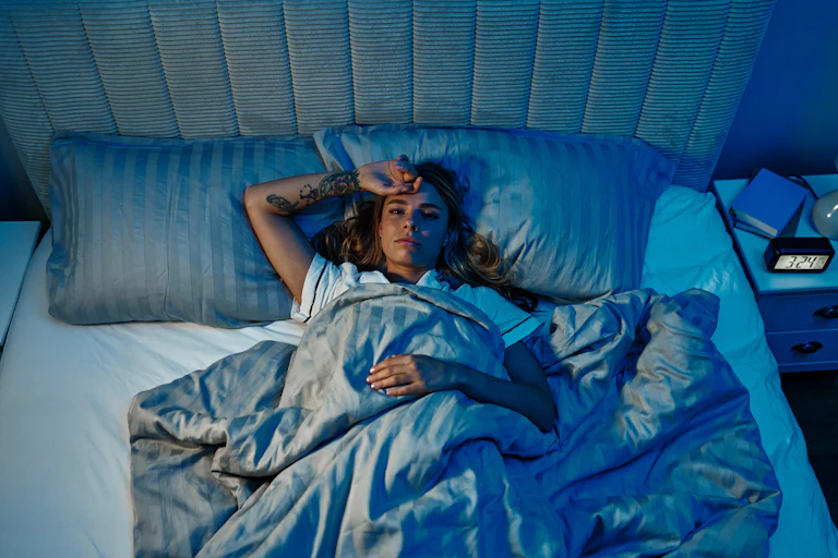 A woman lying face up and awake in bed in the dark, apparently experiencing insomnia.