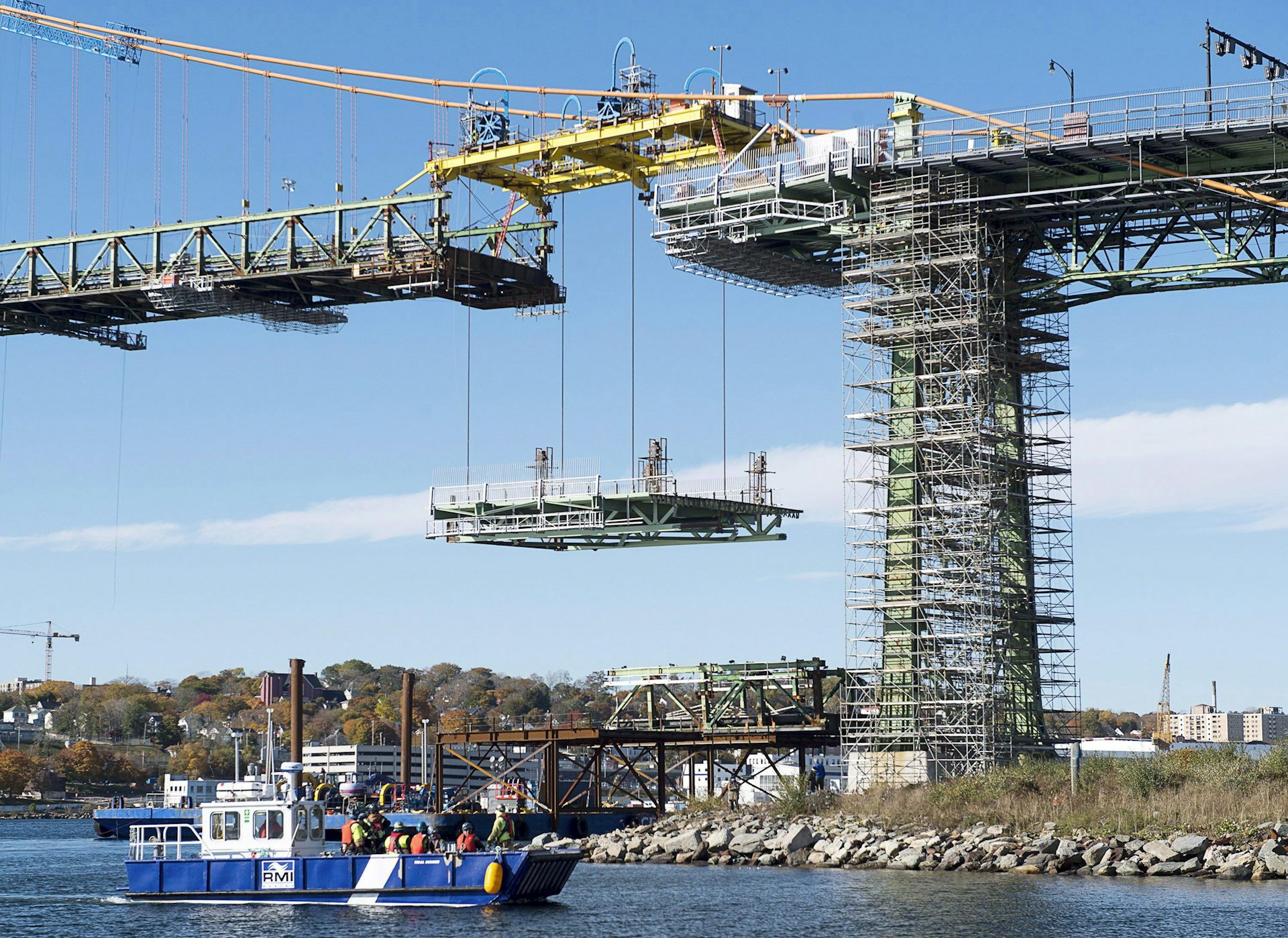 A section of a bridge hangs in the air suspended by an overhead hoist.