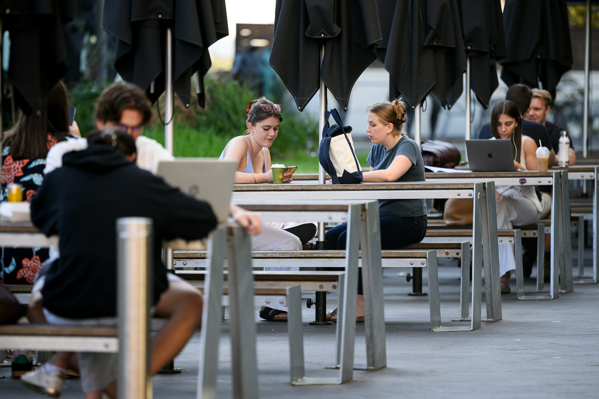 Young people sit with laptops at outdoor benches at Sydney University. 