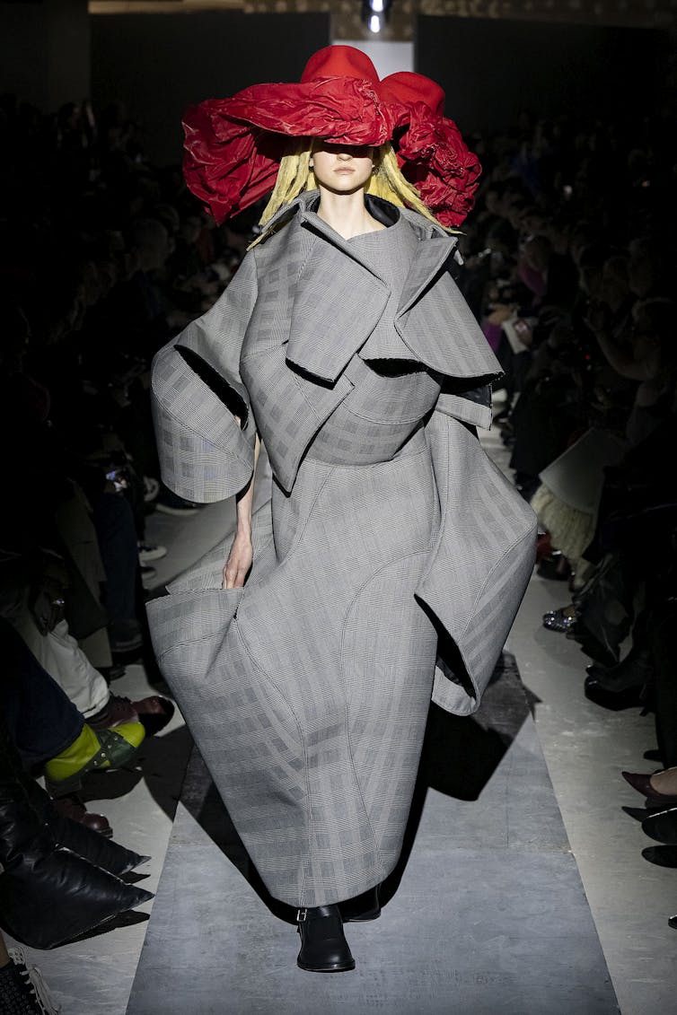 A model in a red hat and a structural grey coat.