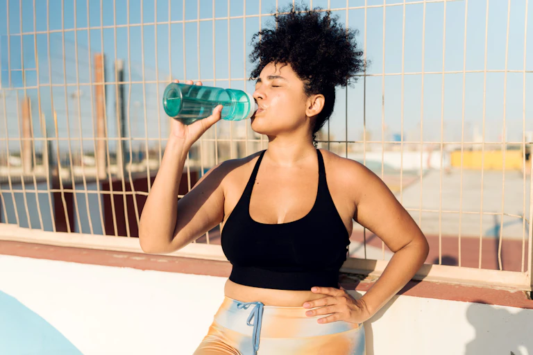 Woman pauses exercise to drink from water bottle.