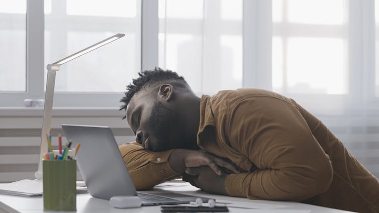 Overworked man sleeping in front of laptop.