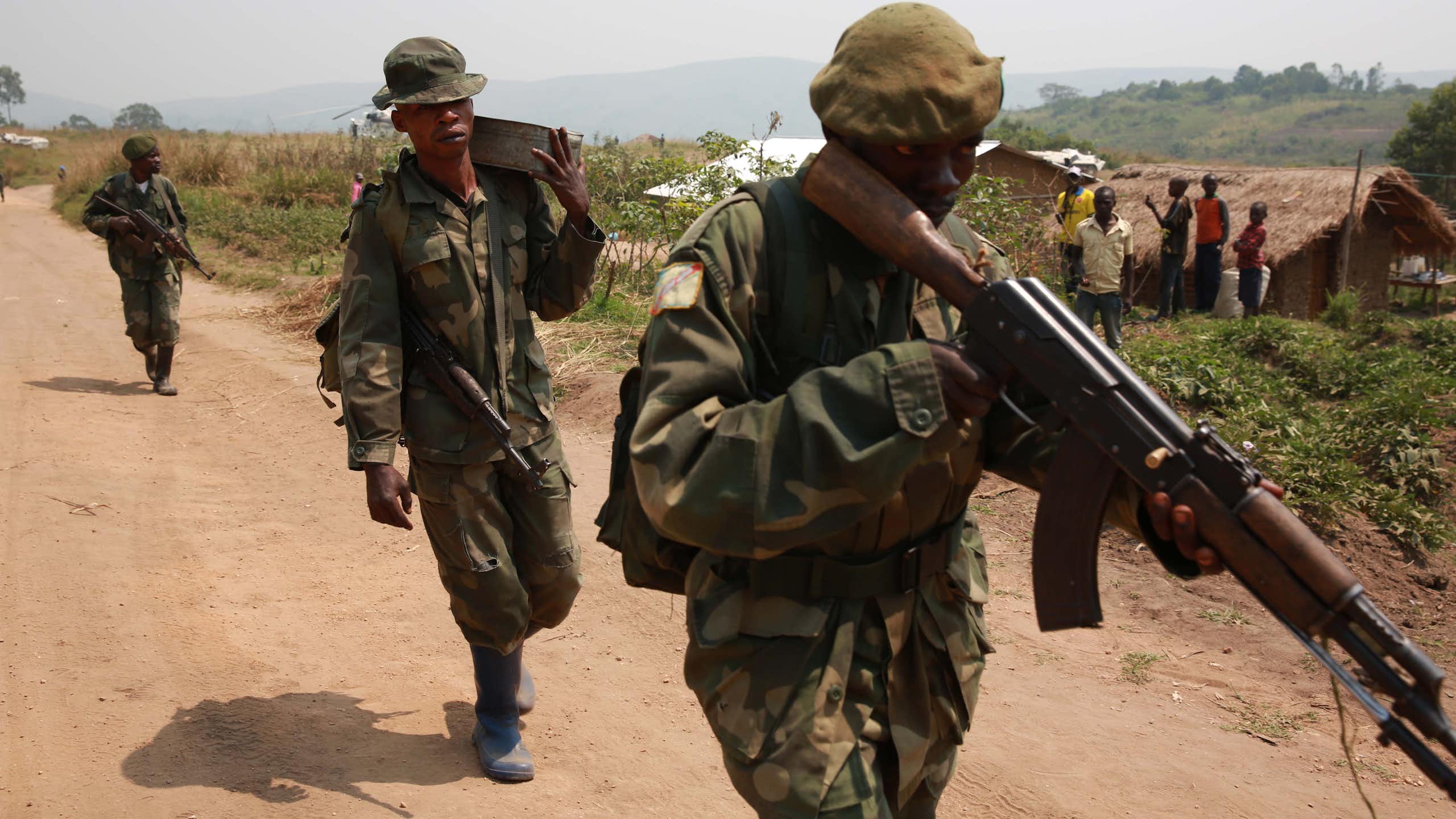 Armed soldiers on foot patrol on a dust road near a rural settlement