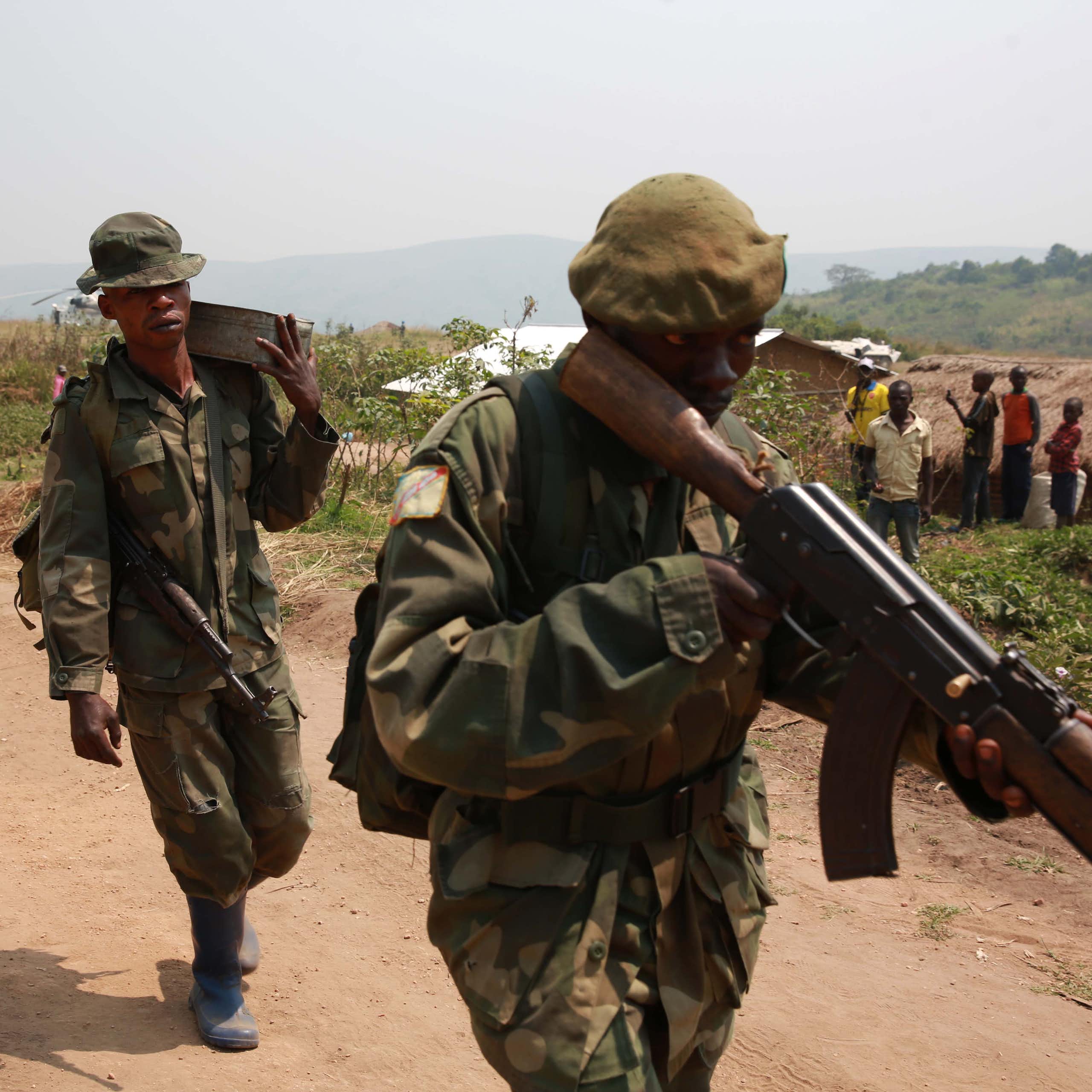 Armed soldiers on foot patrol on a dust road near a rural settlement