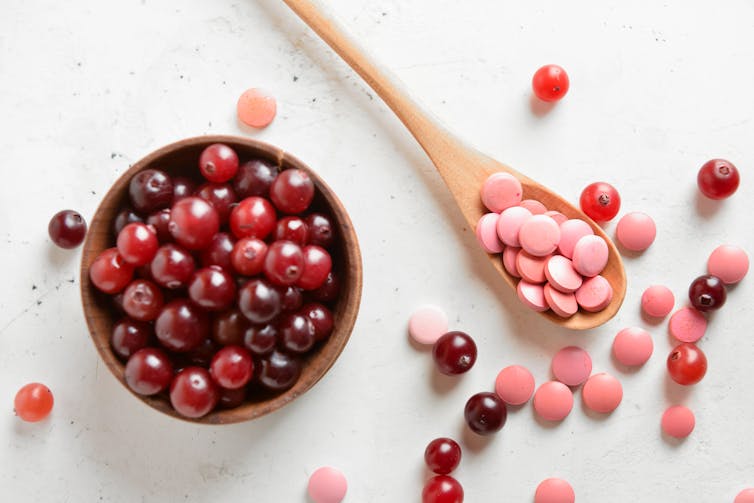 Wooden spoon with cranberry supplements and fresh cranberries in a bowl berries