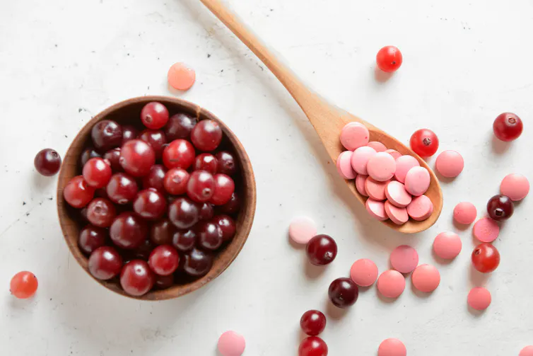 Wooden spoon with cranberry supplements and fresh cranberries in a bowl berries