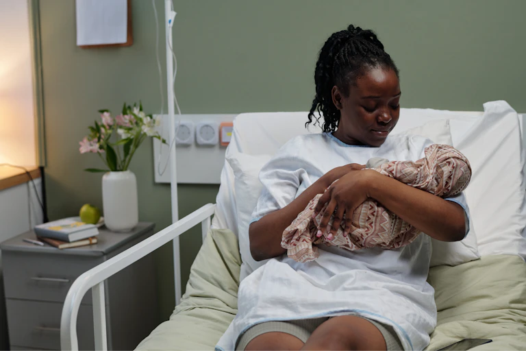 Woman in hospital bed cuddles newborn