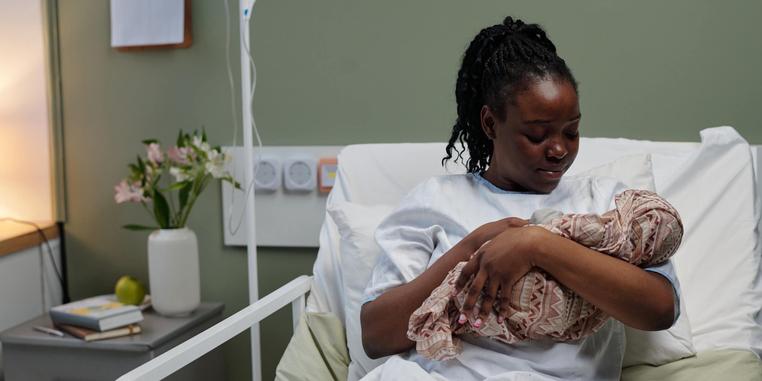 Woman in hospital bed cuddles newborn