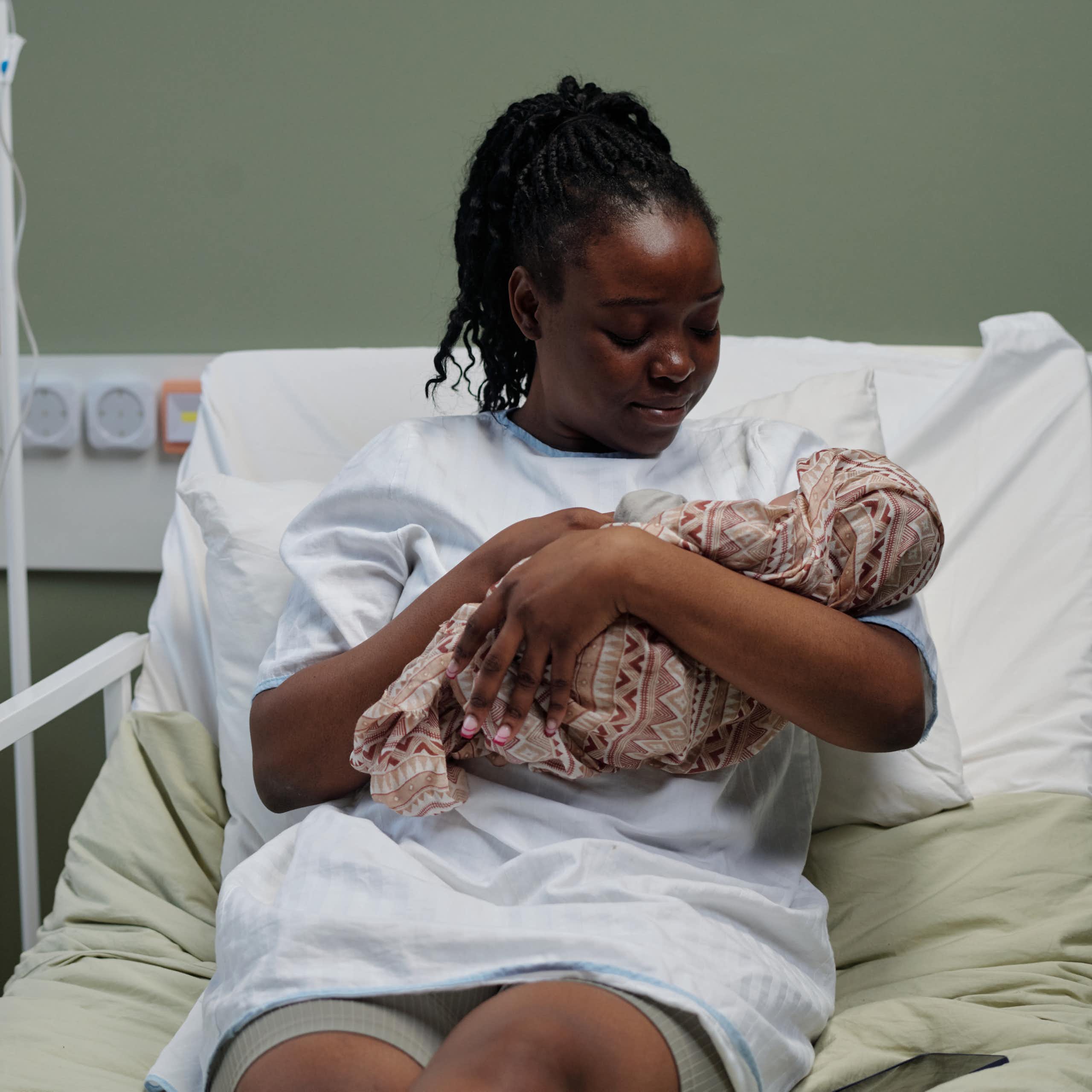 Woman in hospital bed cuddles newborn