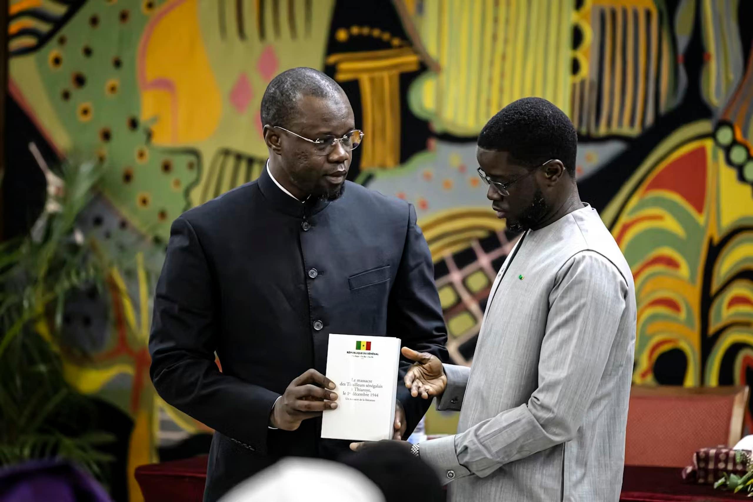 Two African men stand against a colourful art backdrop and hold a document between them.