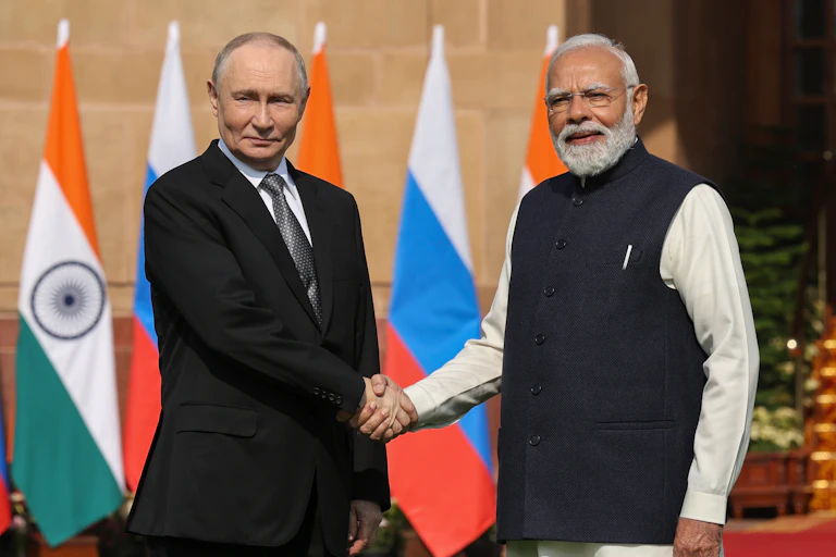 Putin and Modi, outdoors, shake hands in front of a row of Indian and Russian flags
