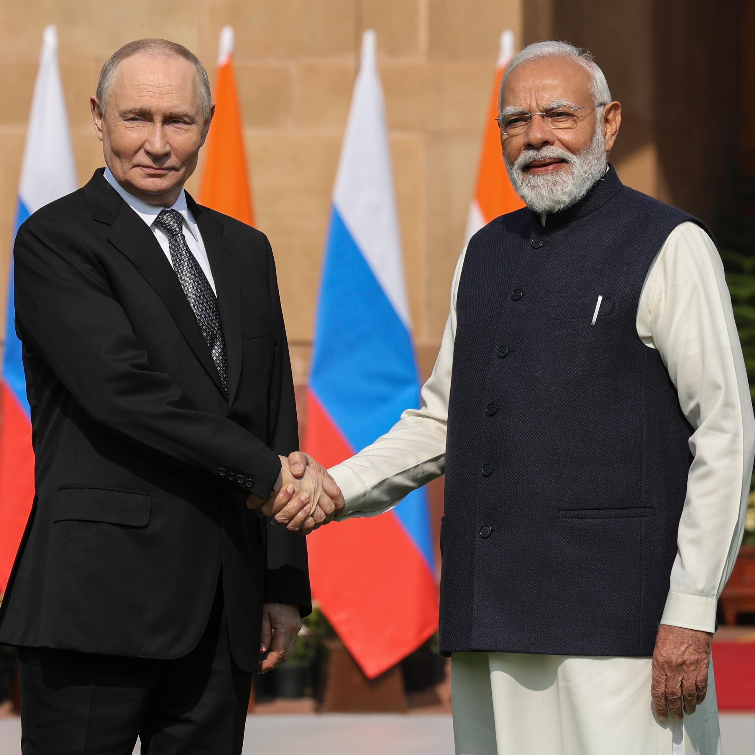 Putin and Modi, outdoors, shake hands in front of a row of Indian and Russian flags