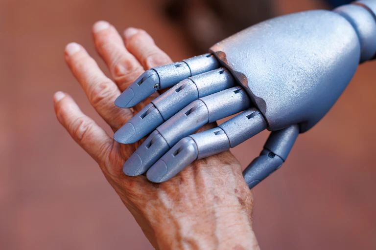 A silver robotic hand holds an old person's hand.