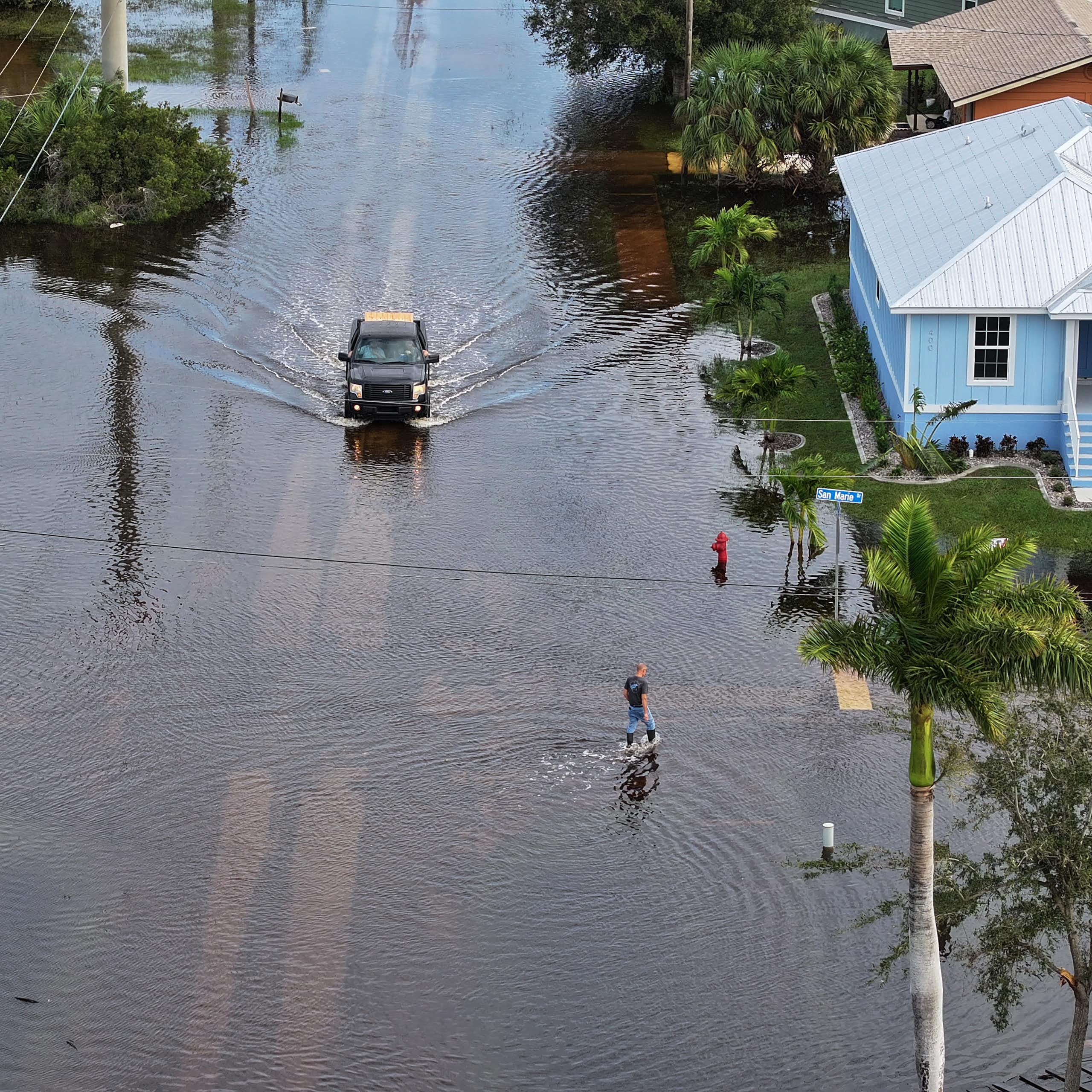 A vehicle drives down a flooded street between houses in Florida.