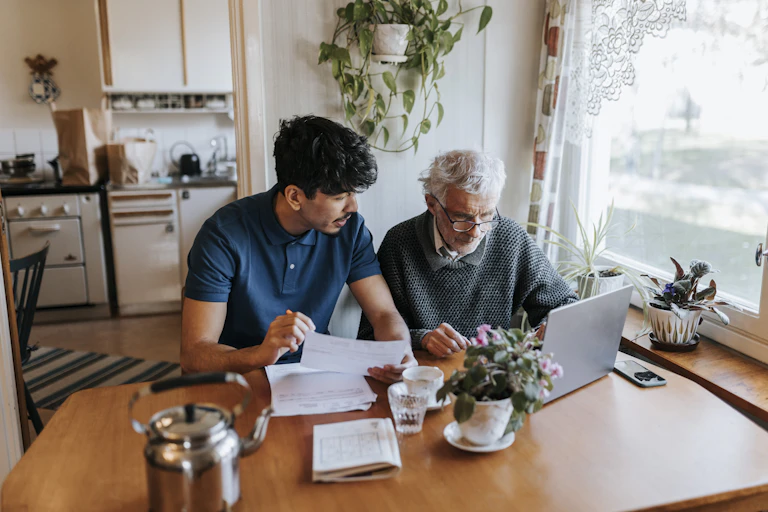 A young man helps an older man navigate technology and papwerwork.