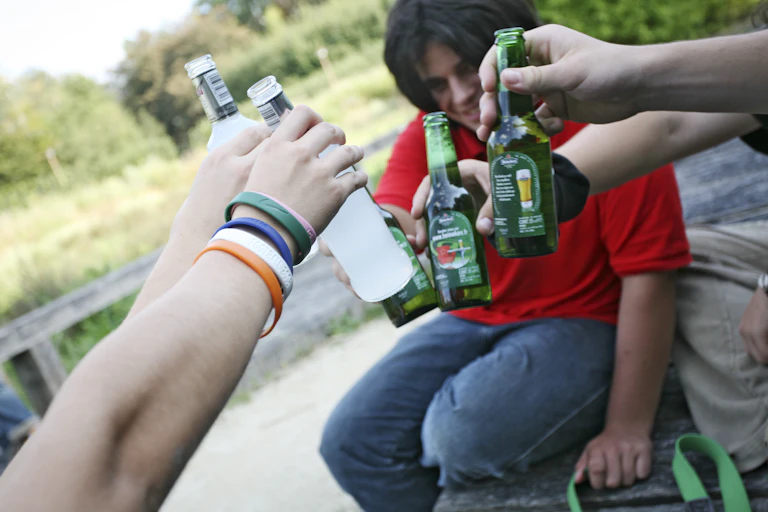 Several people hold glass bottles up for a cheers.