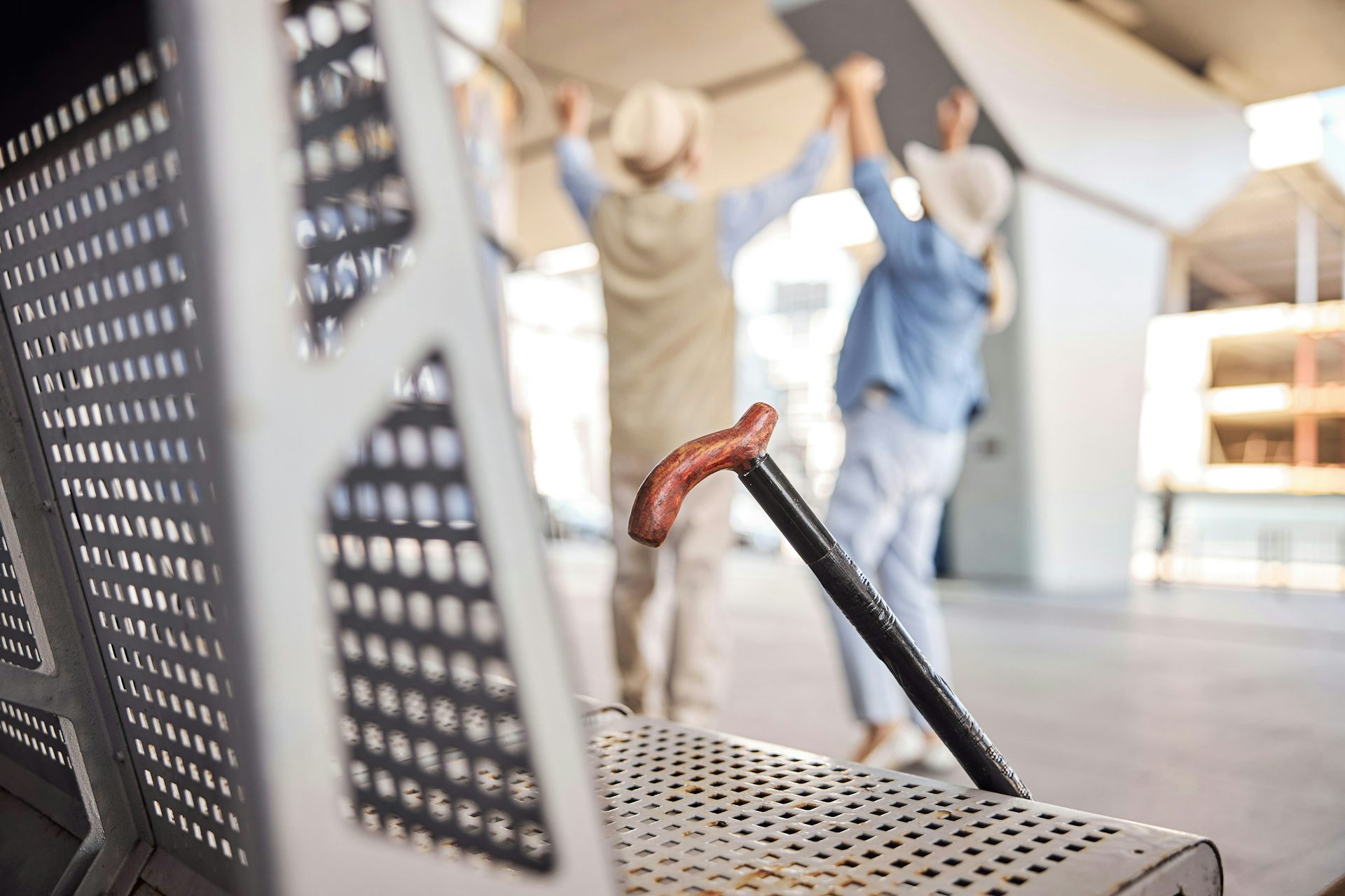 Un bastón descansa sobre un banco mientras dos ancianas permanecen con las manos levantadas a unos metros de distancia.