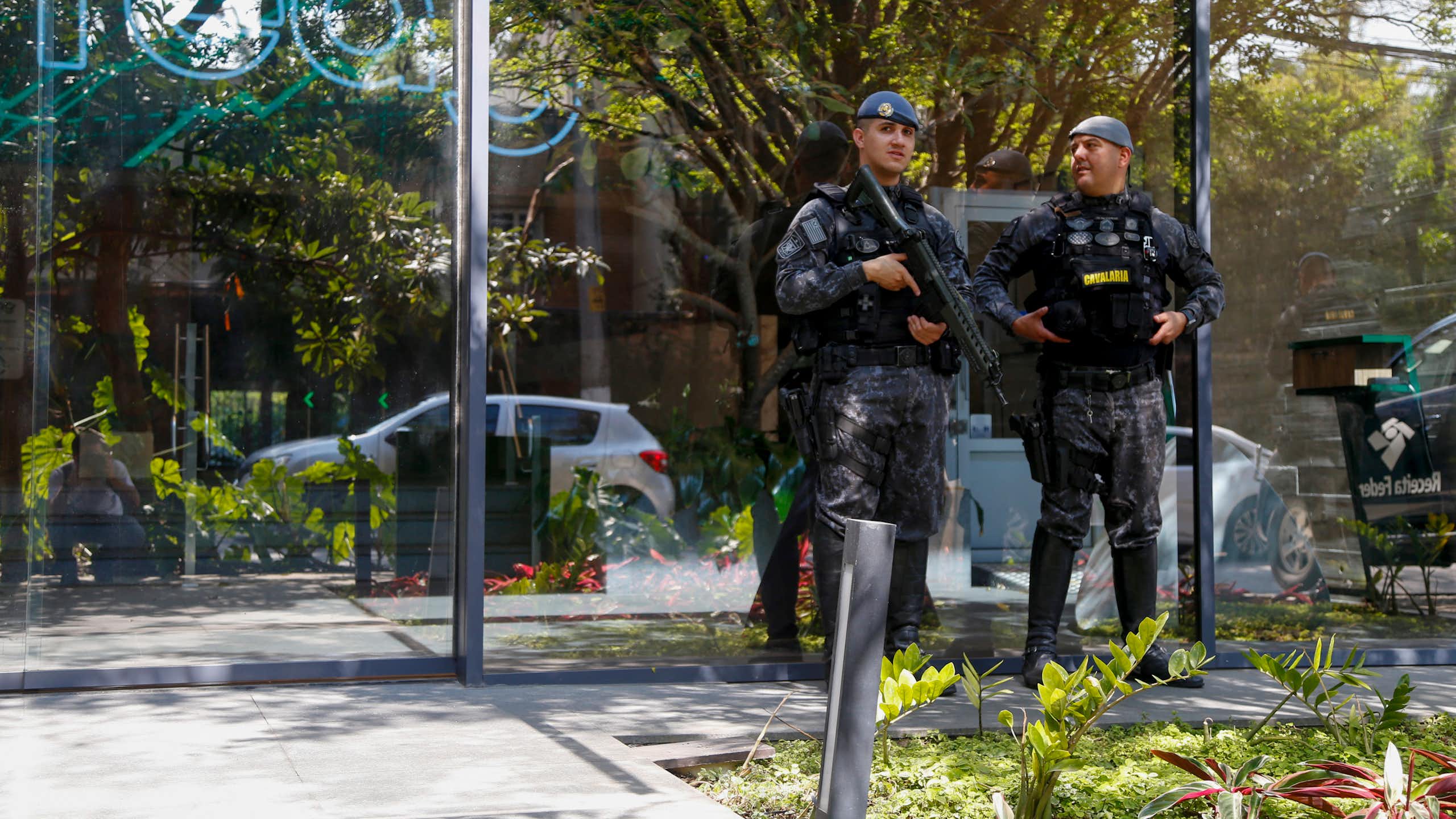 Men in fatigues with guns standf outside a glass building
