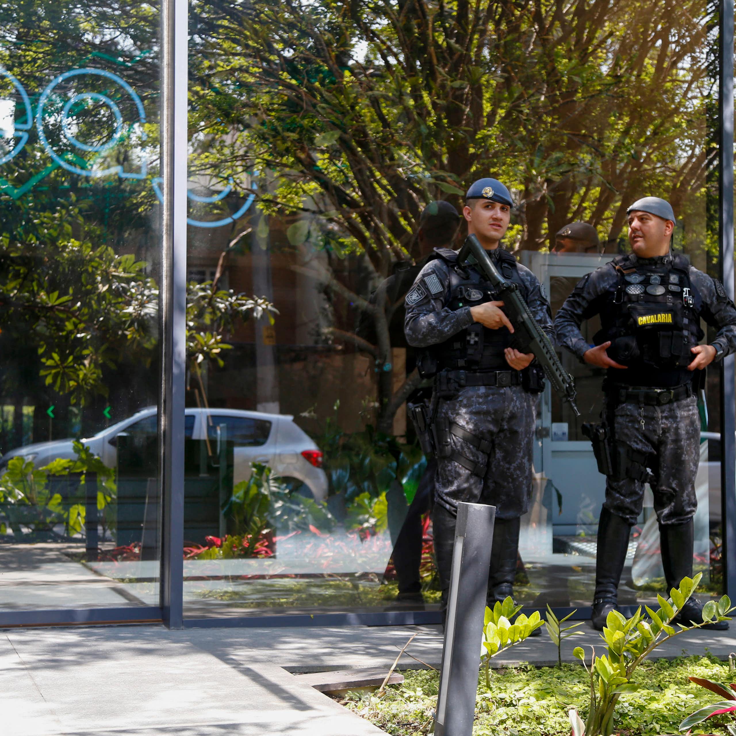 Men in fatigues with guns standf outside a glass building