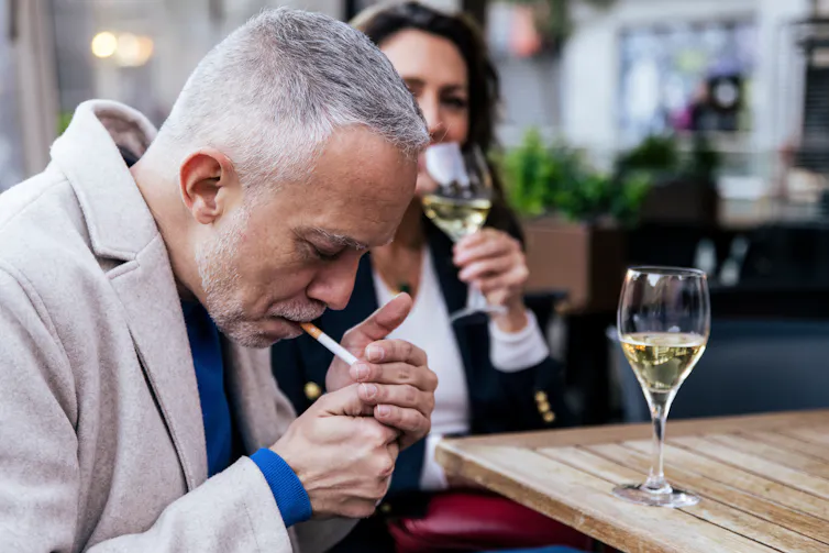 Middle-aged man smoking a cigarette and drinking wine on a terrace with a woman