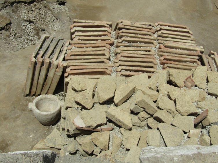 Neatly aligned ceramic roof tiles and tuff blocks at a newly excavated site in Pompeii, documenting the organised storage of building materials ready for reuse during renovation.