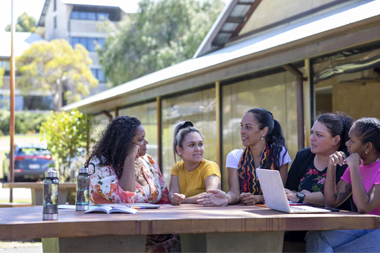 Group of Aboriginal women sitting outside having discussion with laptops and notebooks