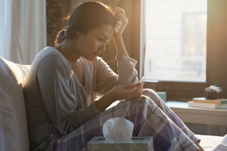 A woman in a casual shirt and pajama pants looks worried as she stares down at a pregnancy test.