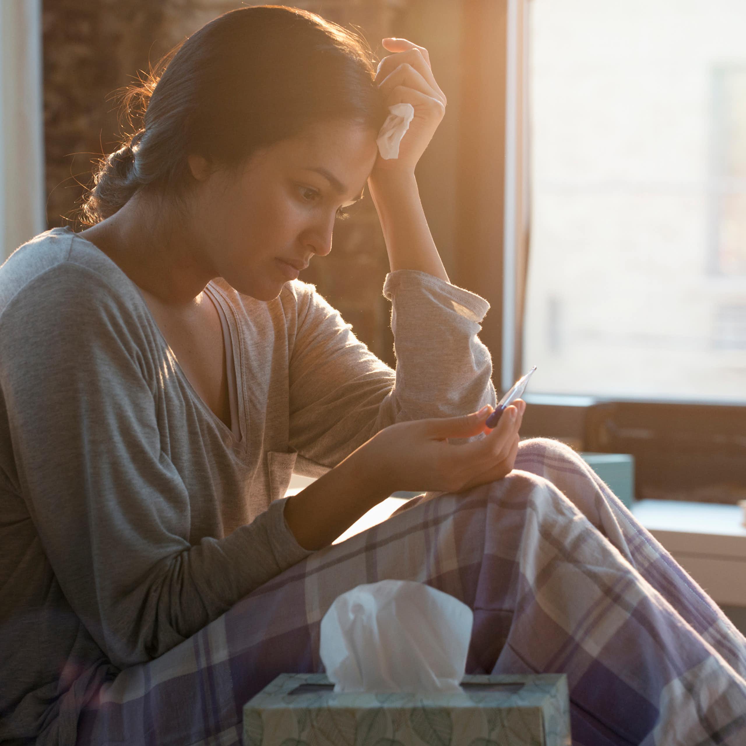 A woman in a casual shirt and pajama pants looks worried as she stares down at a pregnancy test.