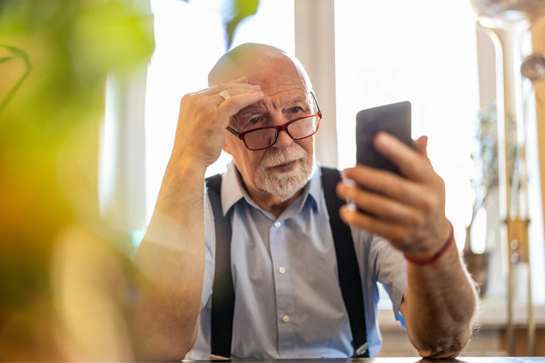 An older man looking at his phone in confusion.