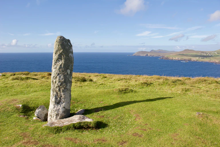 A long thin stone in a green field next to the sea.