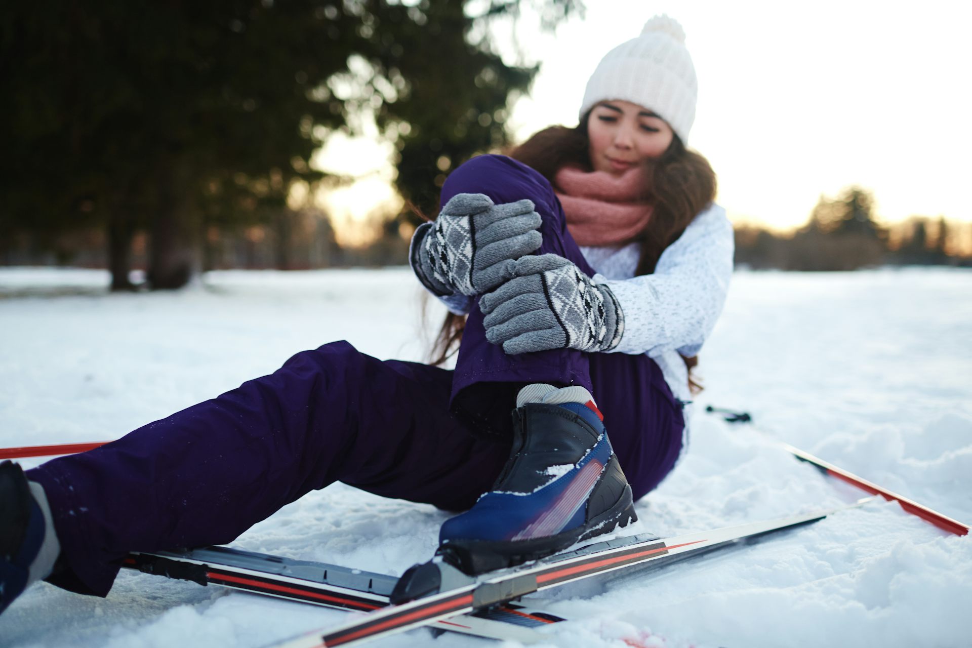 A female skier sits on the ground, with her hands wrapped around her leg.