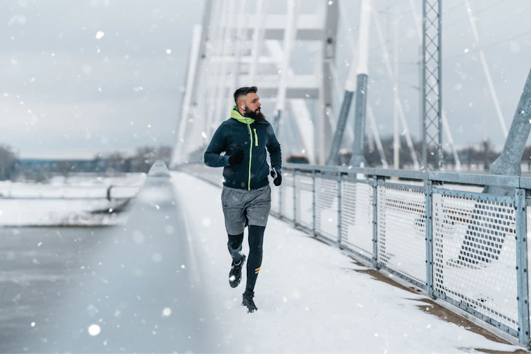 A man goes for a run outdoors across a snowy bridge.