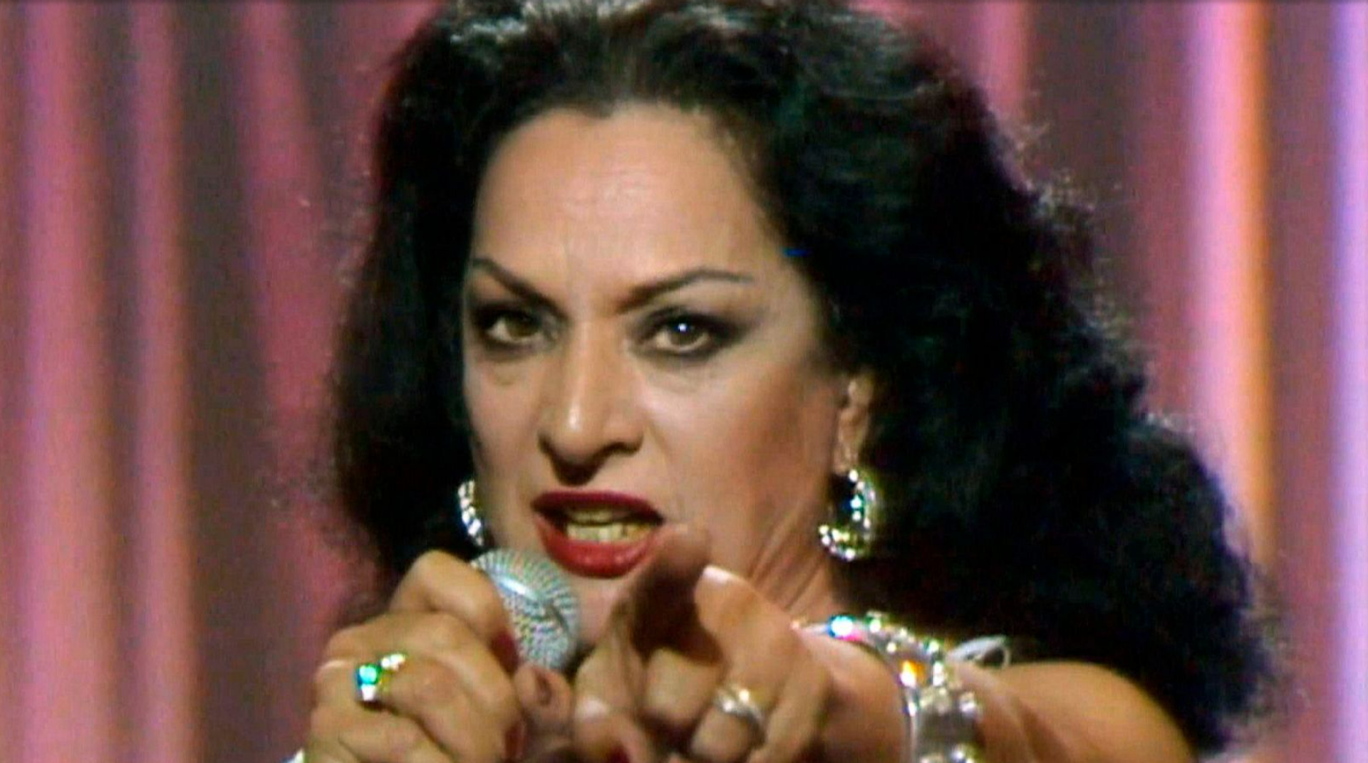 Una mujer cantando señalando a la cámara.