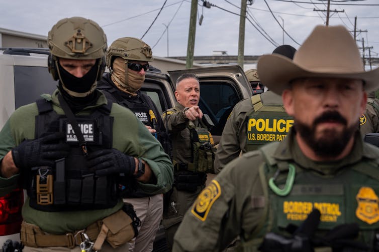 Men dressed in military gear stand near a car.