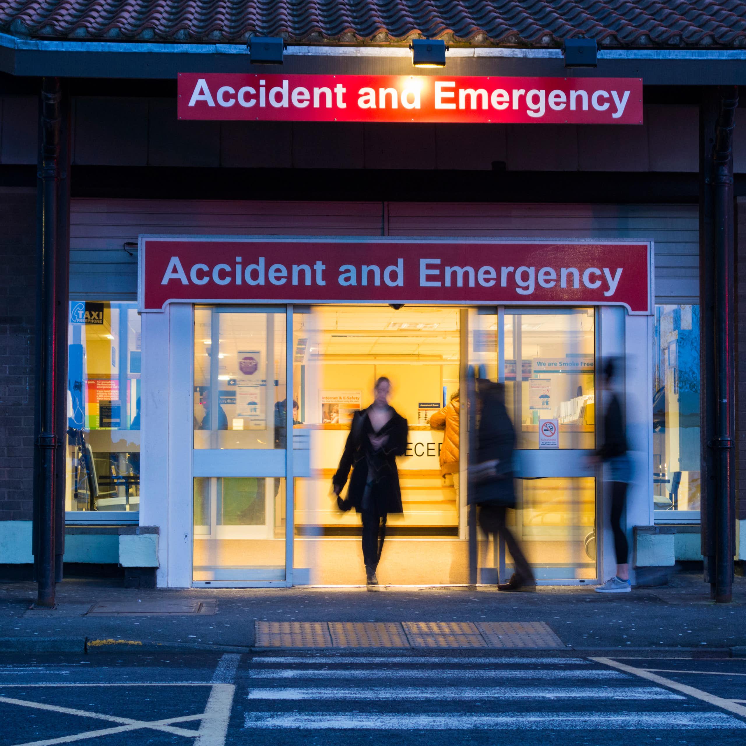 The doors of an A&E at night. People are blurred to hide their identities.