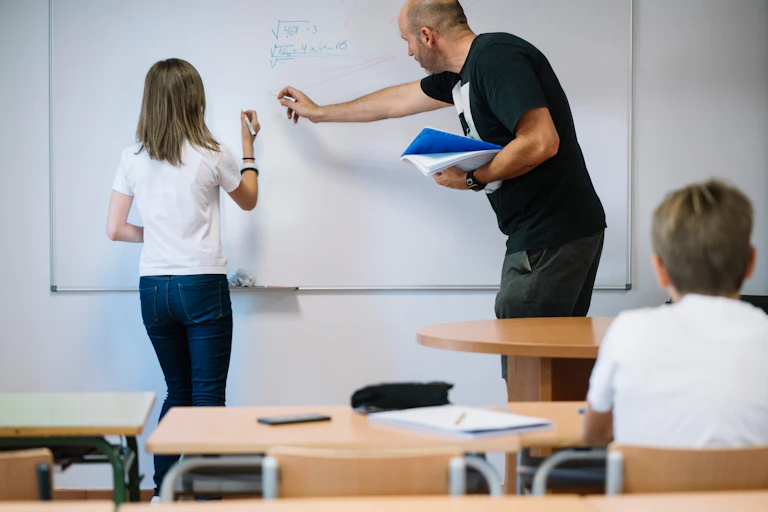 Una niña con un profesor haciendo ejercicios de matemáticas en una pizarra.