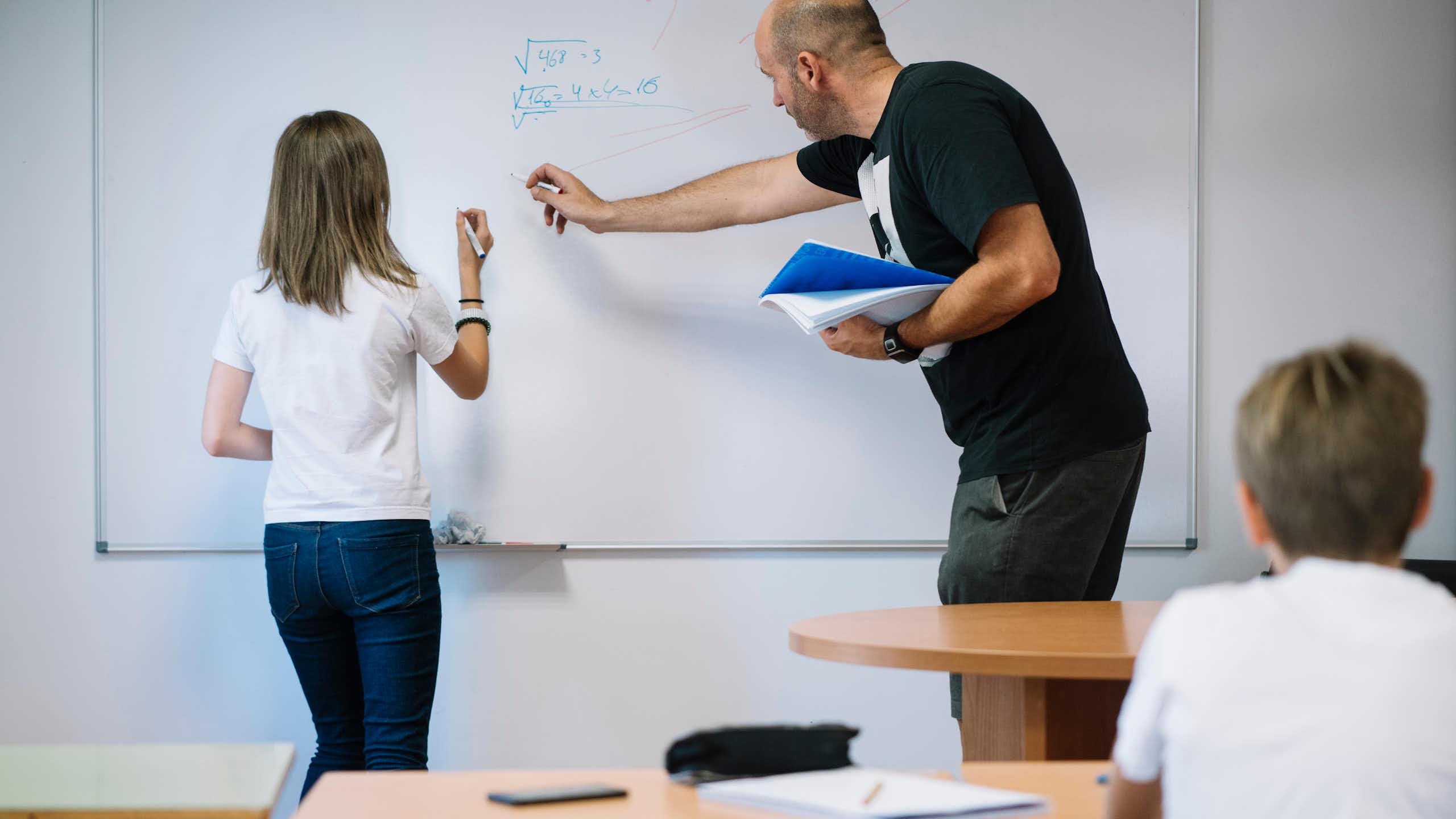 Una niña con un profesor haciendo ejercicios de matemáticas en una pizarra.