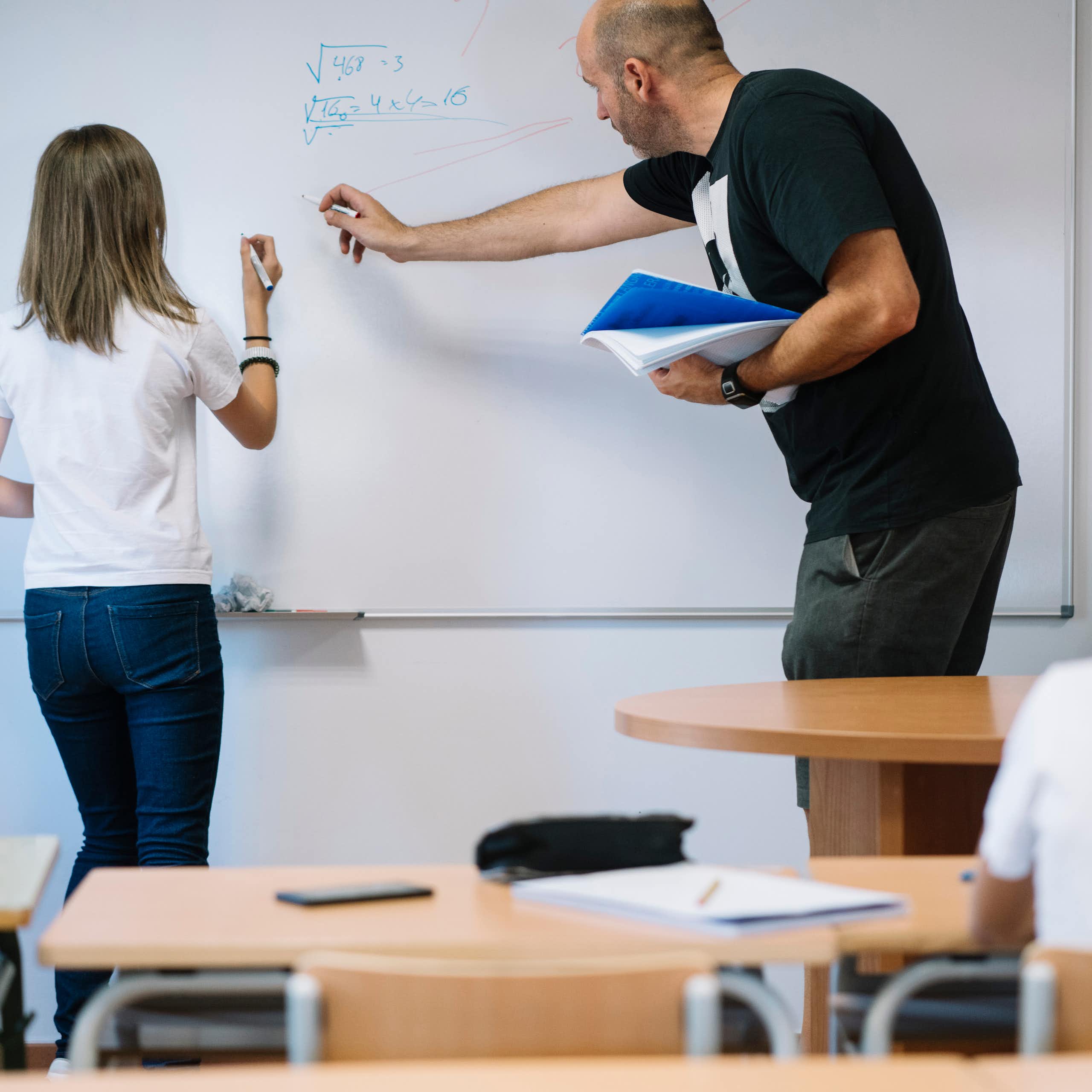 Una niña con un profesor haciendo ejercicios de matemáticas en una pizarra.