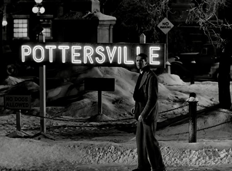 Movie still of young man walking through a dark, snowy town and passing by a bright sign reading 'Pottersville.'
