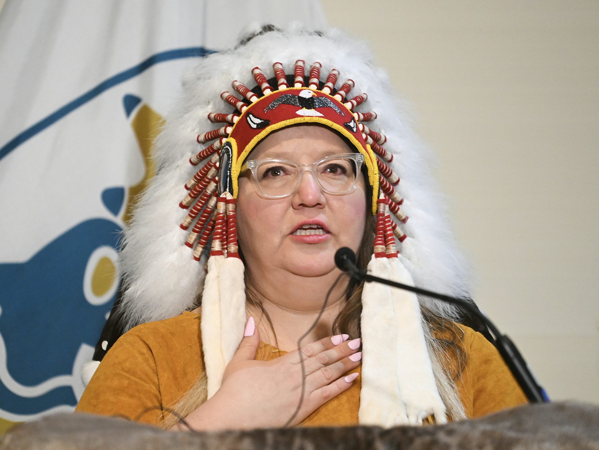 A woman wearing glasses and a headdress speaks into a microphone.